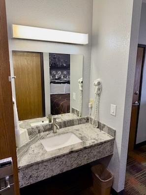 A hotel bathroom with a granite sink, a mirror, a hairdryer, and a towel rack.
