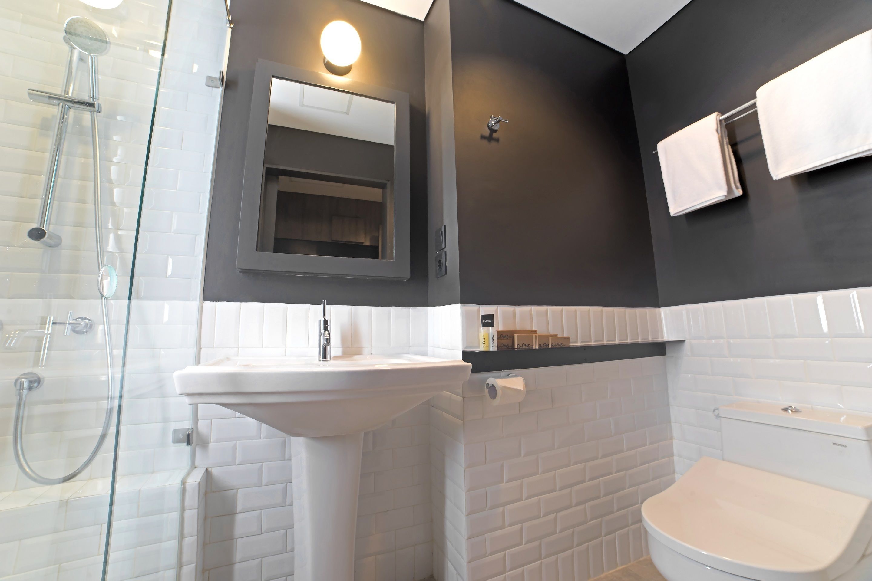 A bathroom with a glass shower enclosure, a white sink, a mirror, and a toilet.