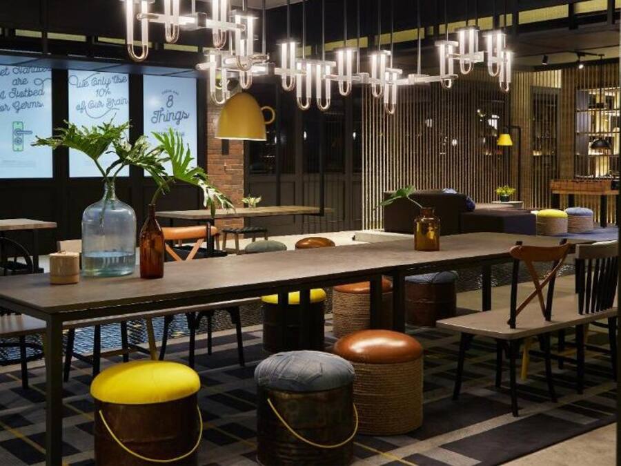 Un restaurante moderno con una larga mesa común, varias zonas de estar y lámparas colgantes.