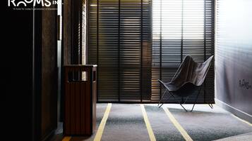 A modern hotel lobby with a metal-framed chair, a trash bin, and a large window with blinds.
