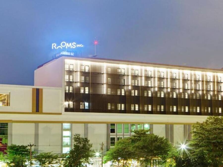 Un moderno edificio de hotel con un letrero destacado que dice “ROOMS INC.” y una fachada bien iluminada.