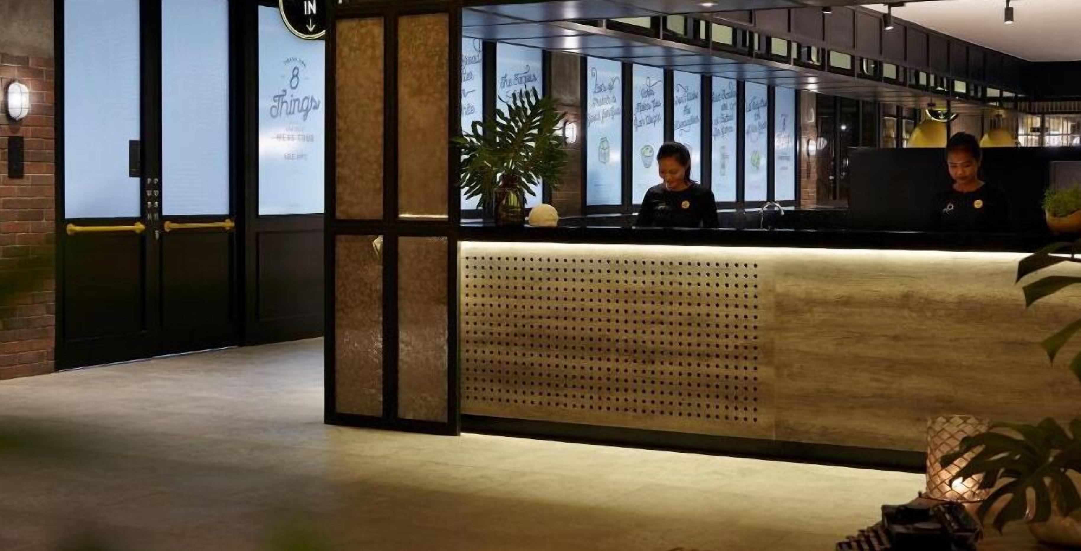 A reception area with a modern design, featuring a reception desk, a large potted plant, and a wall with illuminated signage.