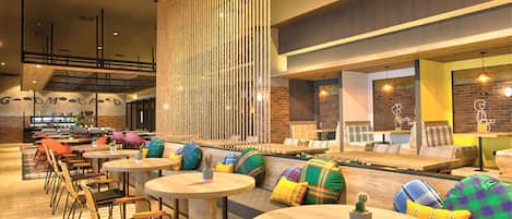 A modern lounge area with round tables, colorful cushions, and a brick wall backdrop.