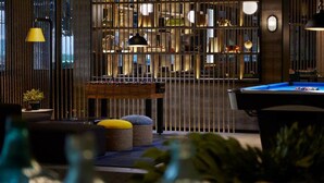 A pool table in a dimly lit room with vertical blinds, a small table with a plant, and a yellow lamp. - Rooms Inc Semarang (Semarang)