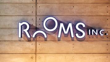 A sign with the text "ROOMS INC." on a wooden wall.