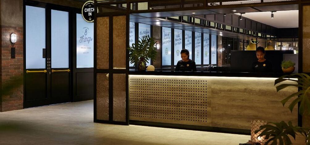 A reception area with a reception desk, two staff members, a clock, and a sign indicating '8 Things to Do in the City'.