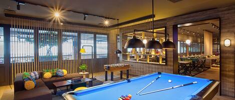 A pool table in a modern living room with a sofa and a table with a pool cue.