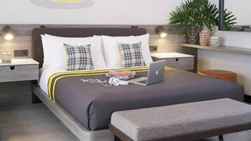 A modern hotel room with a neatly made bed, a laptop, and a bedside table with a lamp.