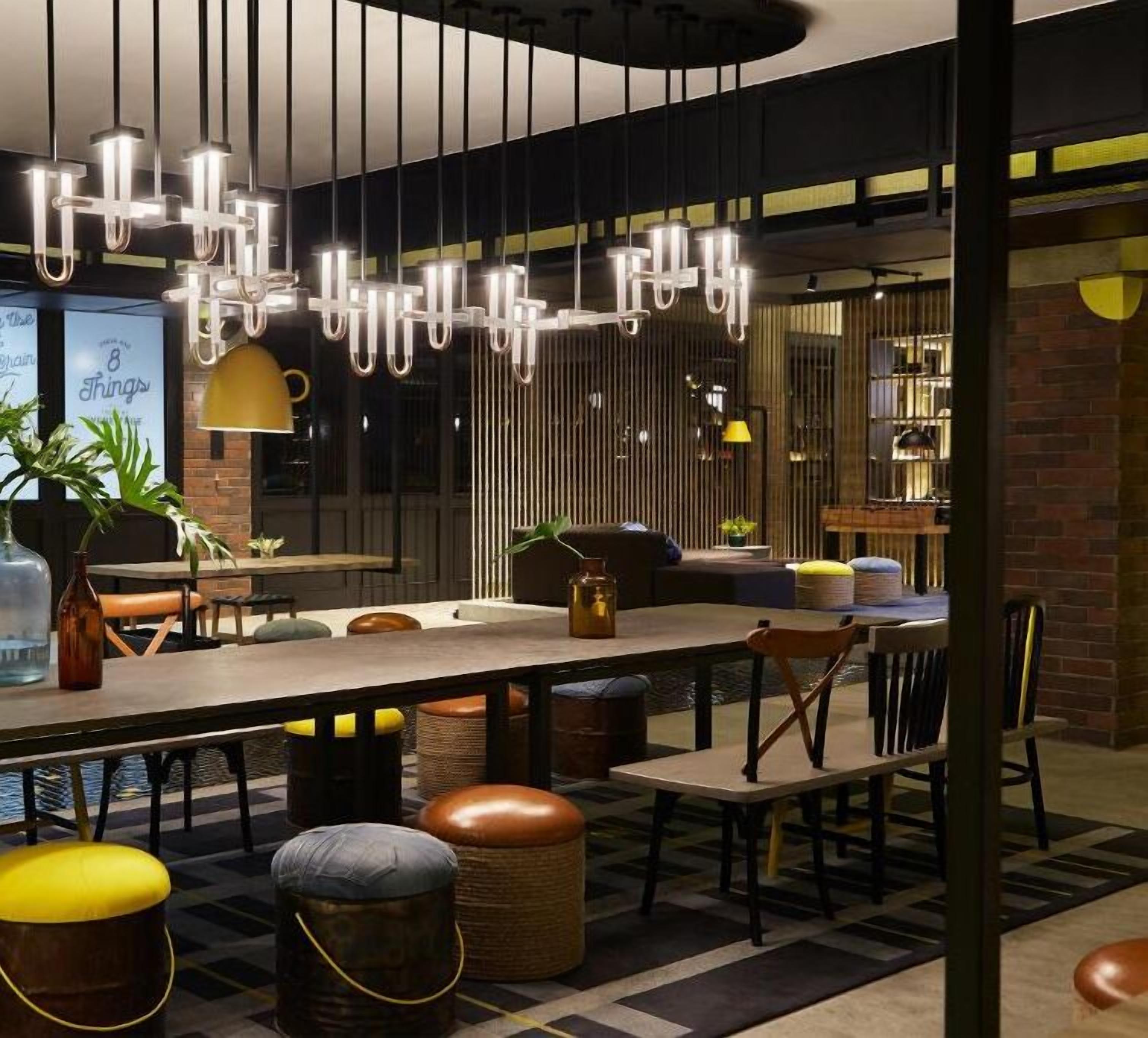 Un espace de salle à manger moderne, doté d’une longue table, de nombreuses chaises et de luminaires suspendus.