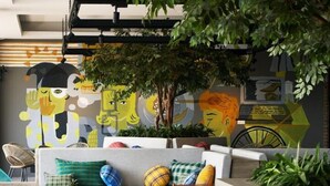A modern living room with a sofa, coffee table, and chairs, featuring a mural and indoor plants. - Rooms Inc Semarang (Semarang)