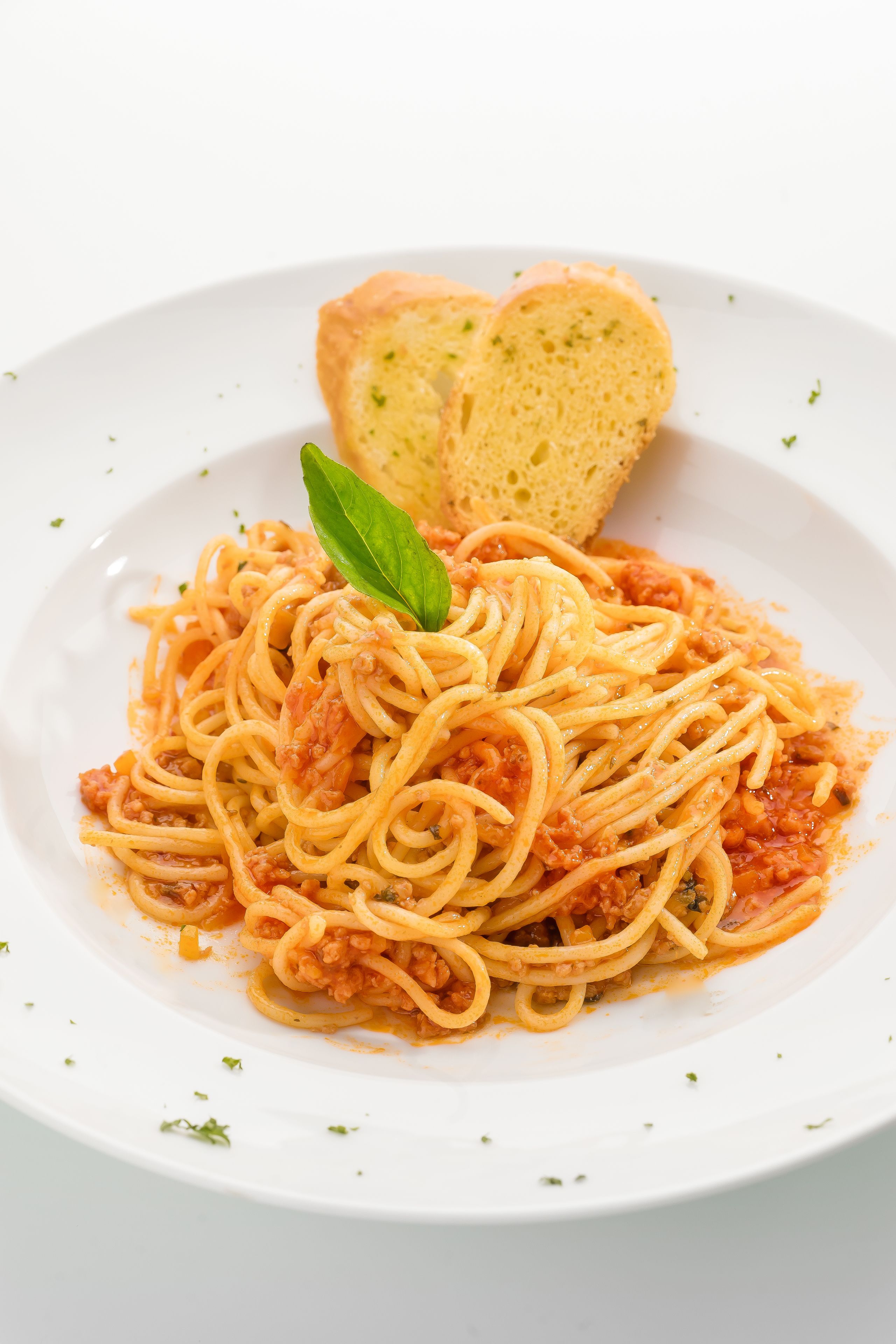 A plate of spaghetti with tomato sauce and a basil leaf, accompanied by a slice of bread.