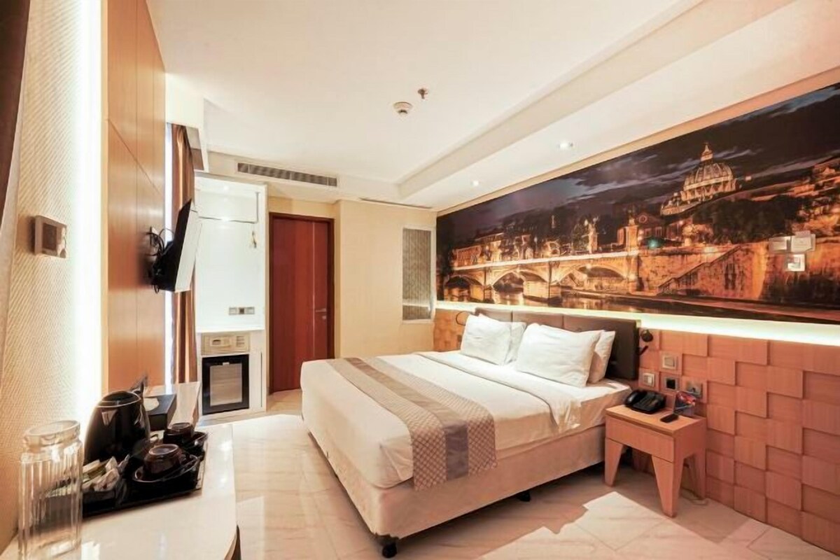 A hotel room with a large bed, a flat-screen TV, a small desk with a chair, and a wall-mounted TV.