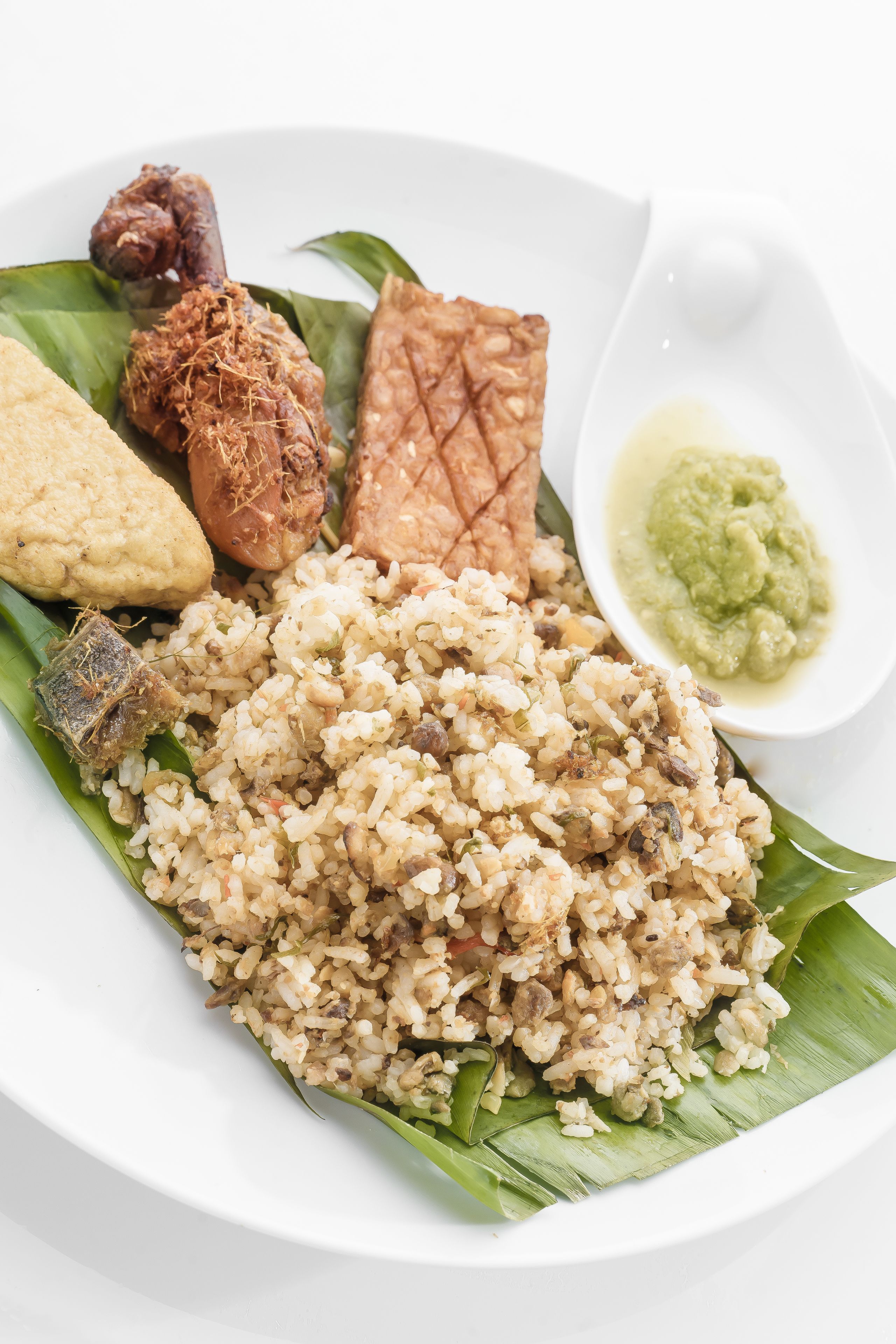 A plate of food with rice, fish, and a side of green sauce.