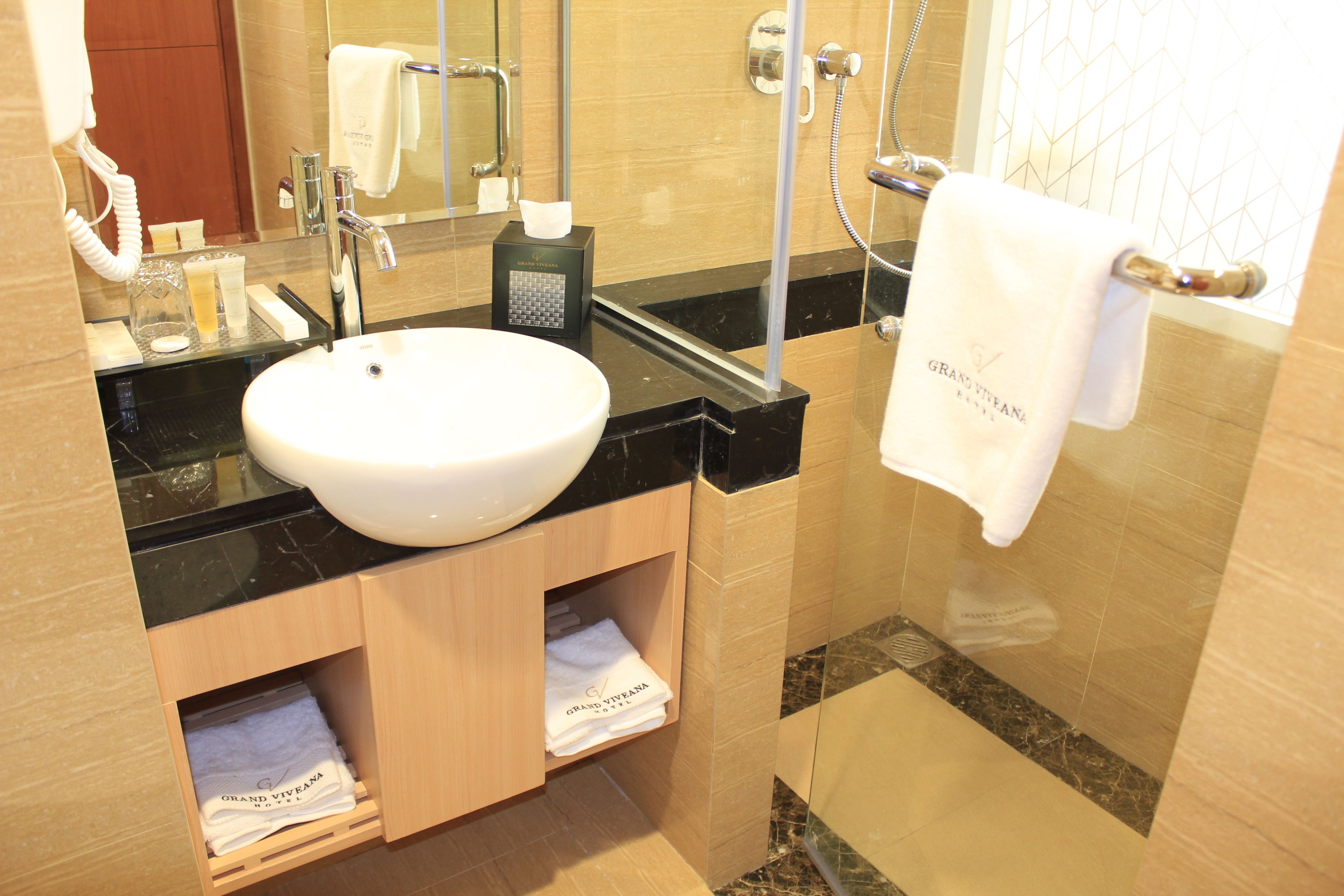 A bathroom with a white sink, black countertop, and wooden cabinets. There is a towel rack with a white towel hanging on it.
