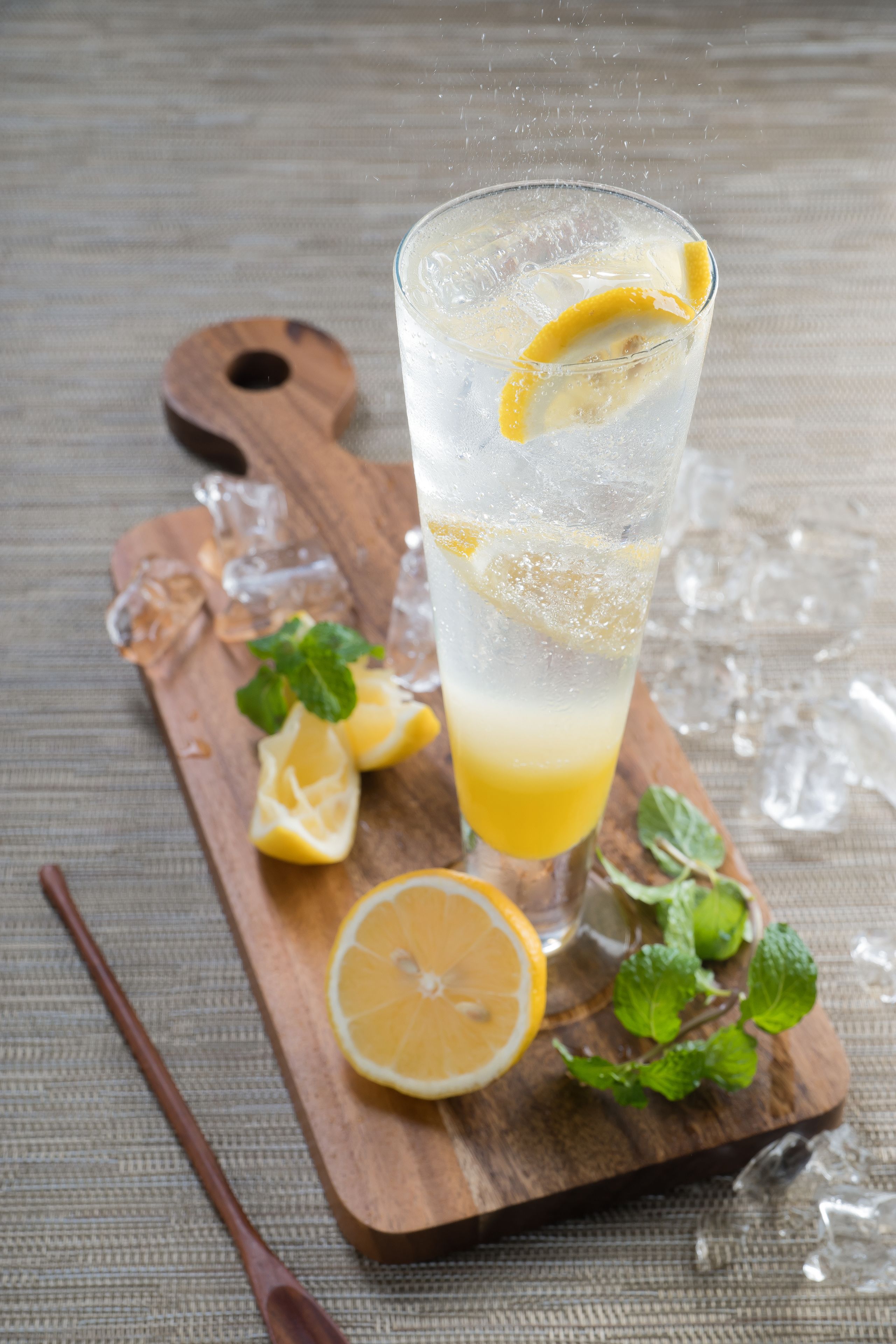A glass of iced beverage with lemon slices and mint leaves on a wooden board.