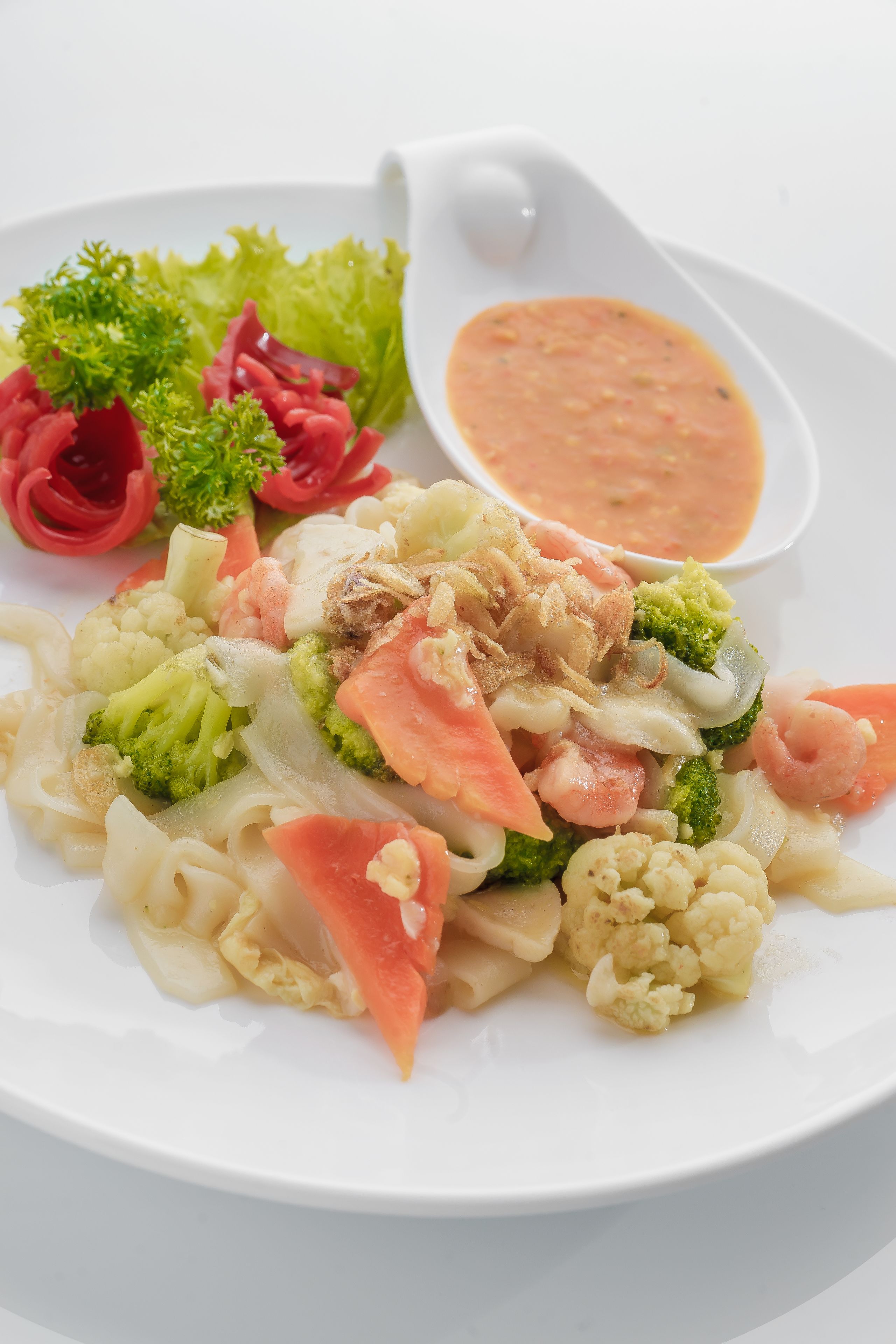 A plate of food with vegetables and shrimp, accompanied by a small bowl of sauce.