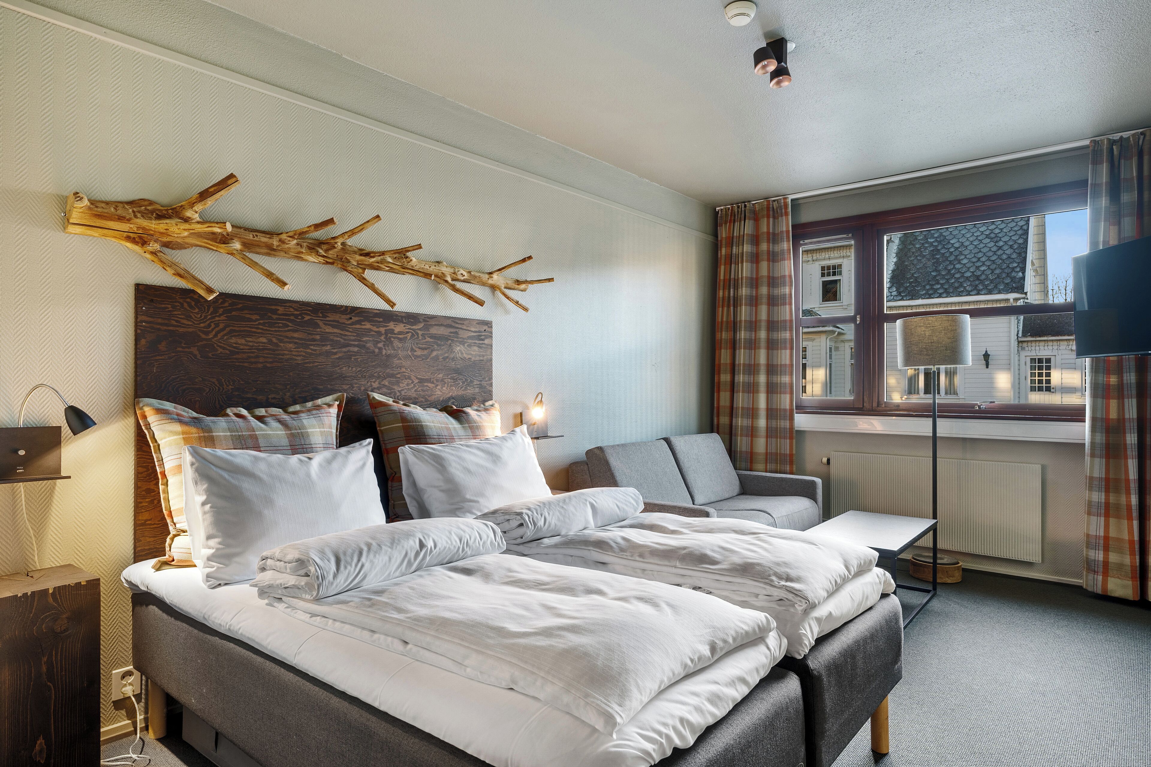 A hotel room with a large bed, a sofa, a TV, and a window with curtains.