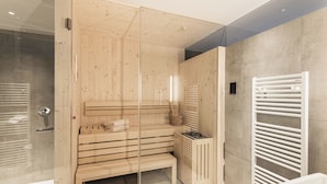 Moderni sauna, jossa on puiset lauteet, pieni kiuas ja lasiseinä.