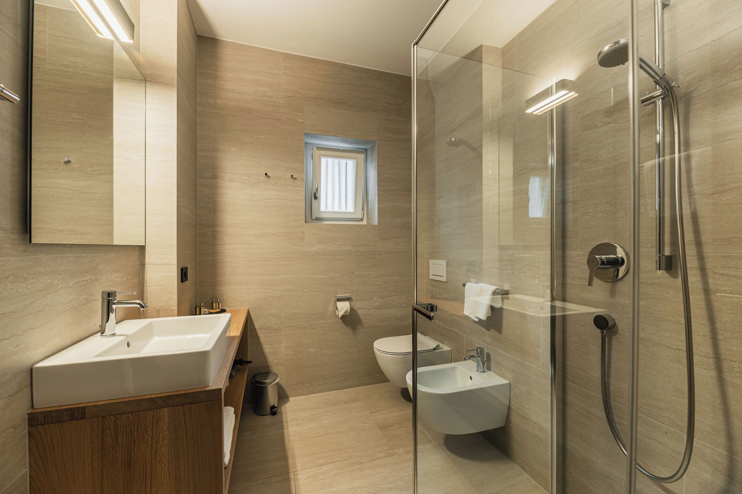 Une salle de bain moderne avec une douche à parois de verre, un grand miroir, un lavabo et un bidet.