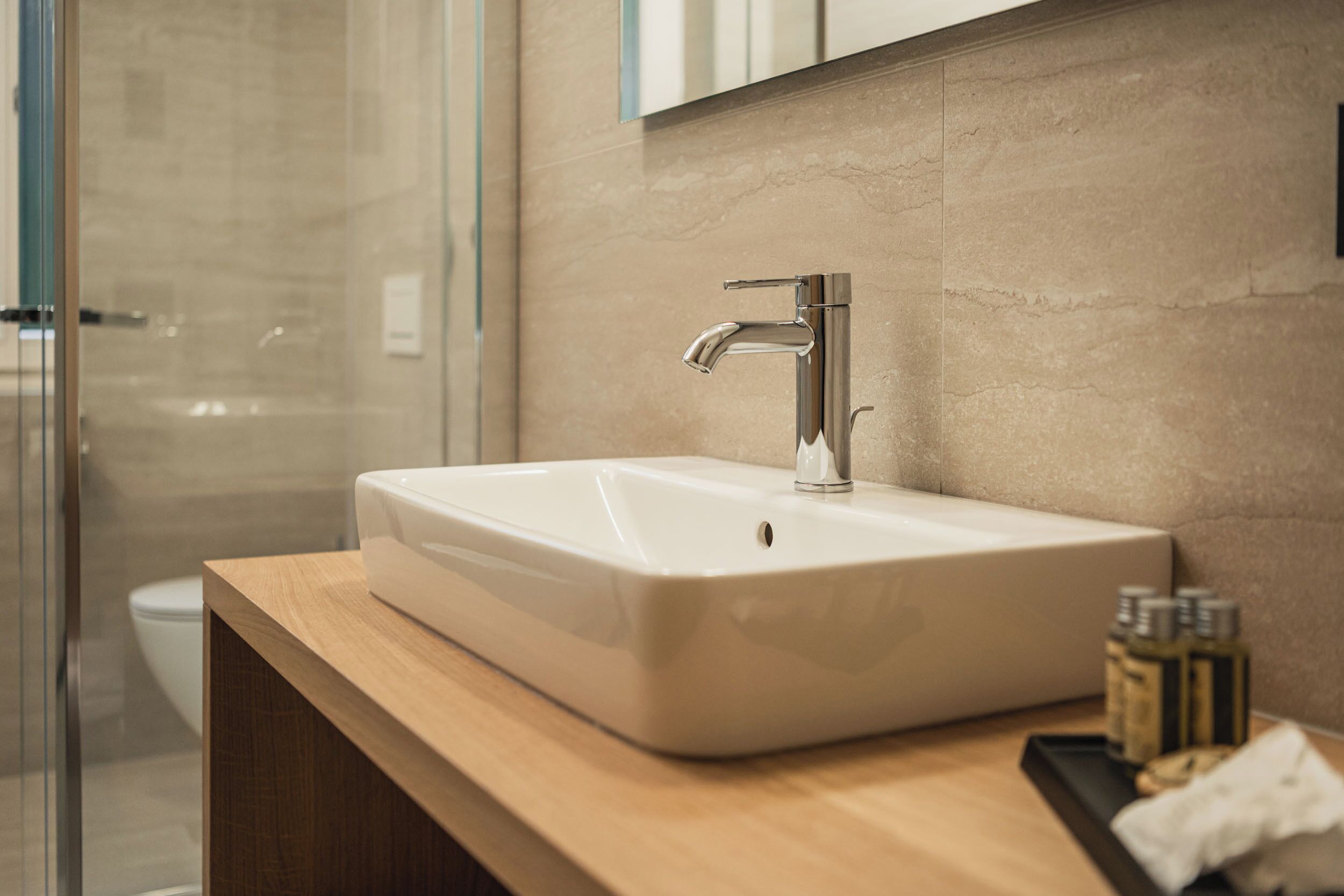 A modern bathroom with a large sink, a glass shower enclosure, and a wooden countertop.