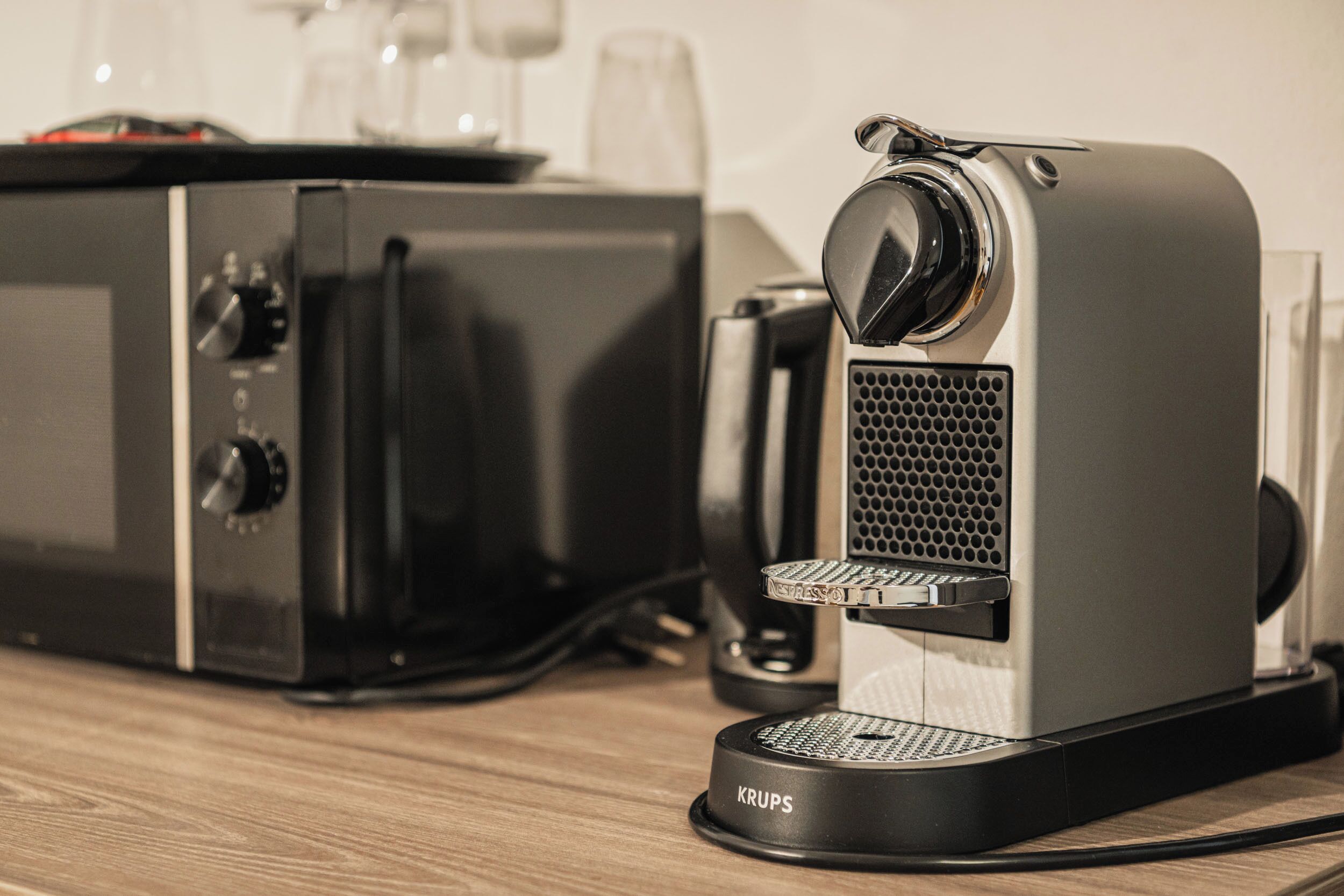 Une machine à expresso Krups, avec un moulin à café, une bouilloire et une cafetière, posée sur une surface en bois.