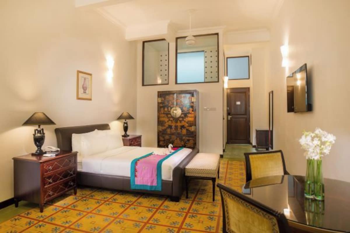A hotel room with a bed, bedside tables, a chair, a small table, and a mirror.