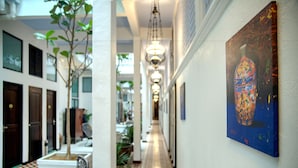 A corridor with a tiled floor, a bench, a potted plant, and a painting on the wall. - Areca Hotel Penang (George Town)