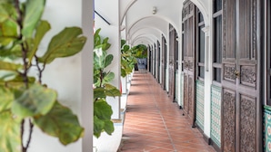 A corridor with white walls, tiled floor, and wooden doors with decorative patterns. - Areca Hotel Penang (George Town)