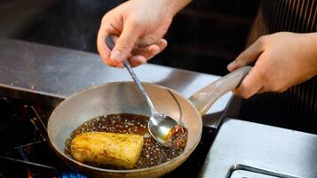 A person cooking a piece of food in a pan on a stove.