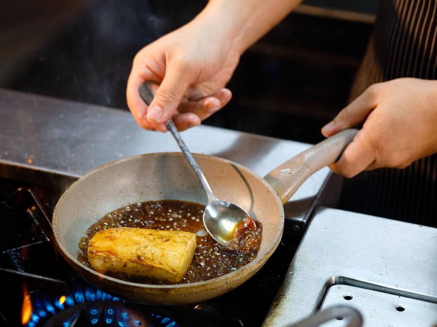 A person cooking a piece of food in a pan on a stove.