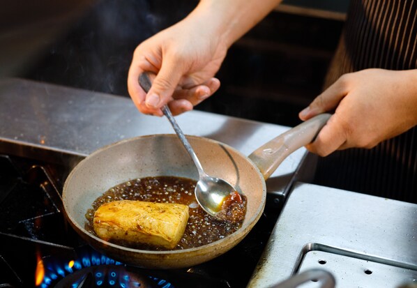 A person cooking a piece of food in a pan on a stove. - Areca Hotel Penang (George Town)
