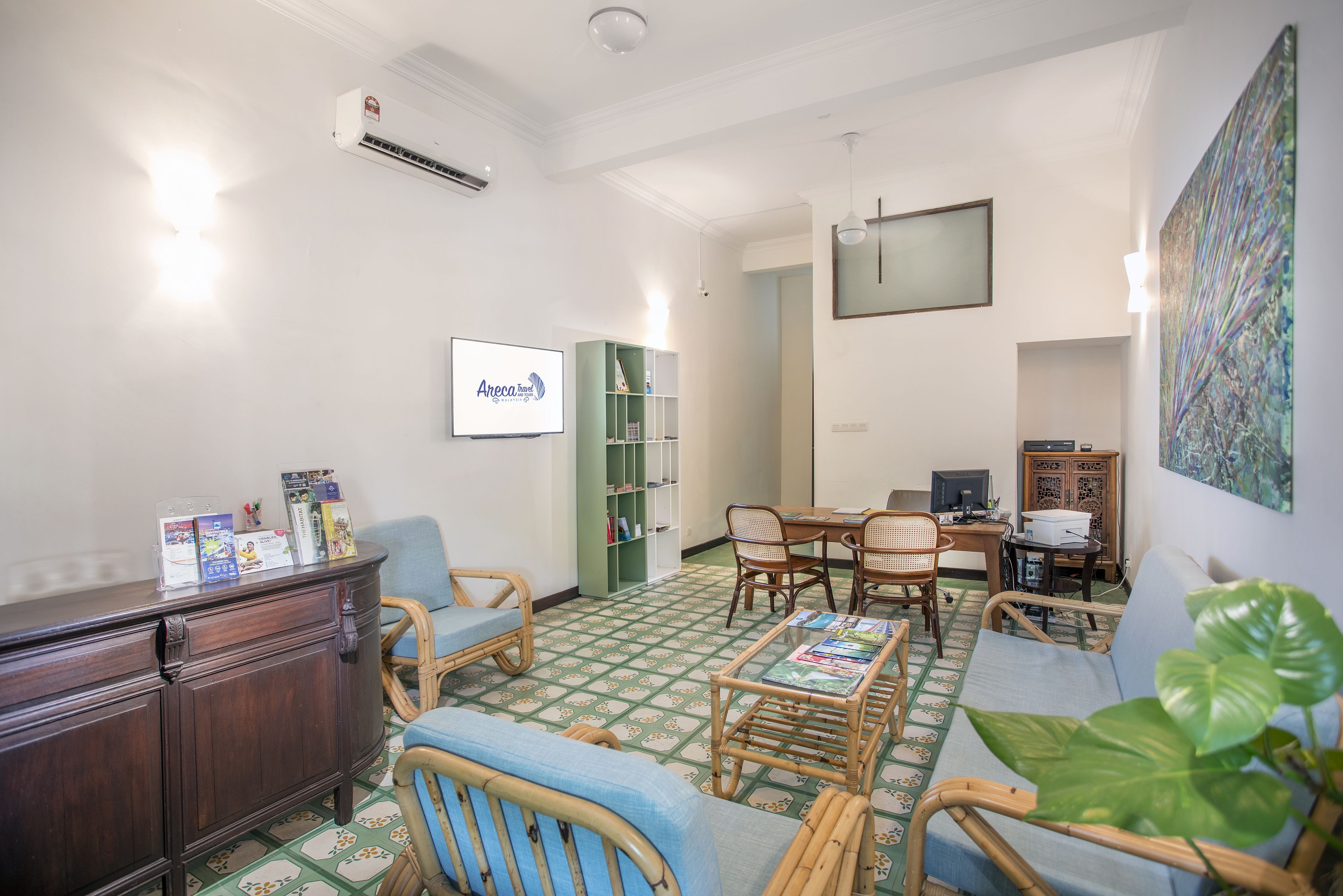 Un salón con piso estampado en verde y blanco, muebles de mimbre, un aparador de madera y una estantería.