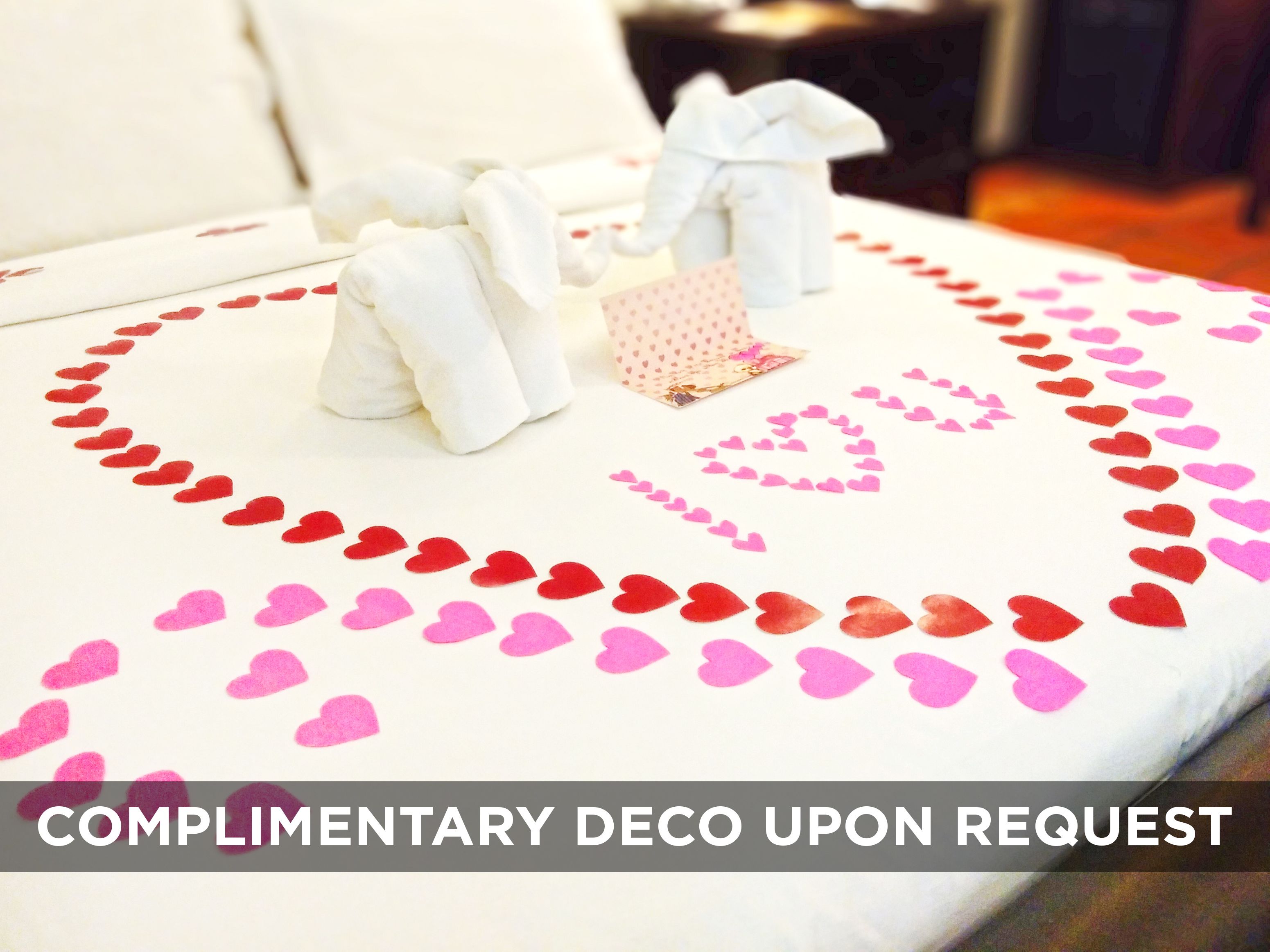 A bed with a white sheet, red and pink heart decorations, and a small gift box.