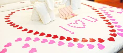 A bed with a white sheet, red and pink heart decorations, and a small gift box.