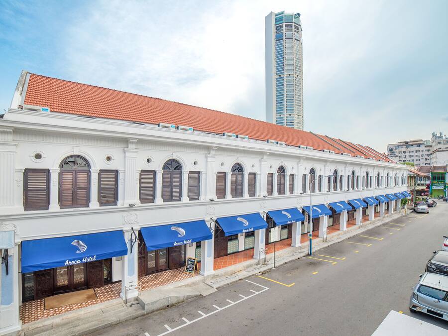 A white building with brown shutters and blue awnings labeled "Areca Hotel."
