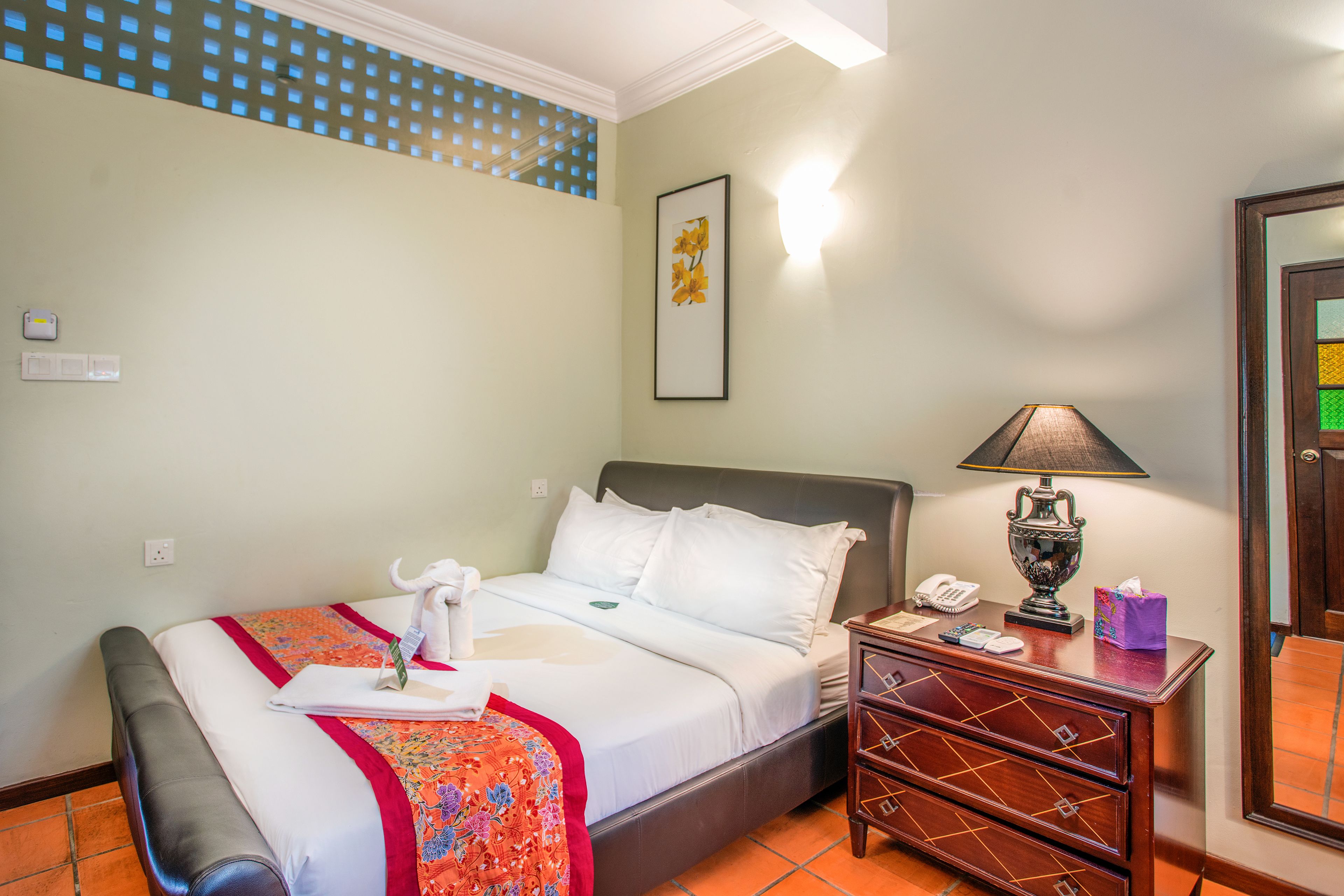 A hotel room with a bed, a bedside table with a lamp, a telephone, and a small cabinet.