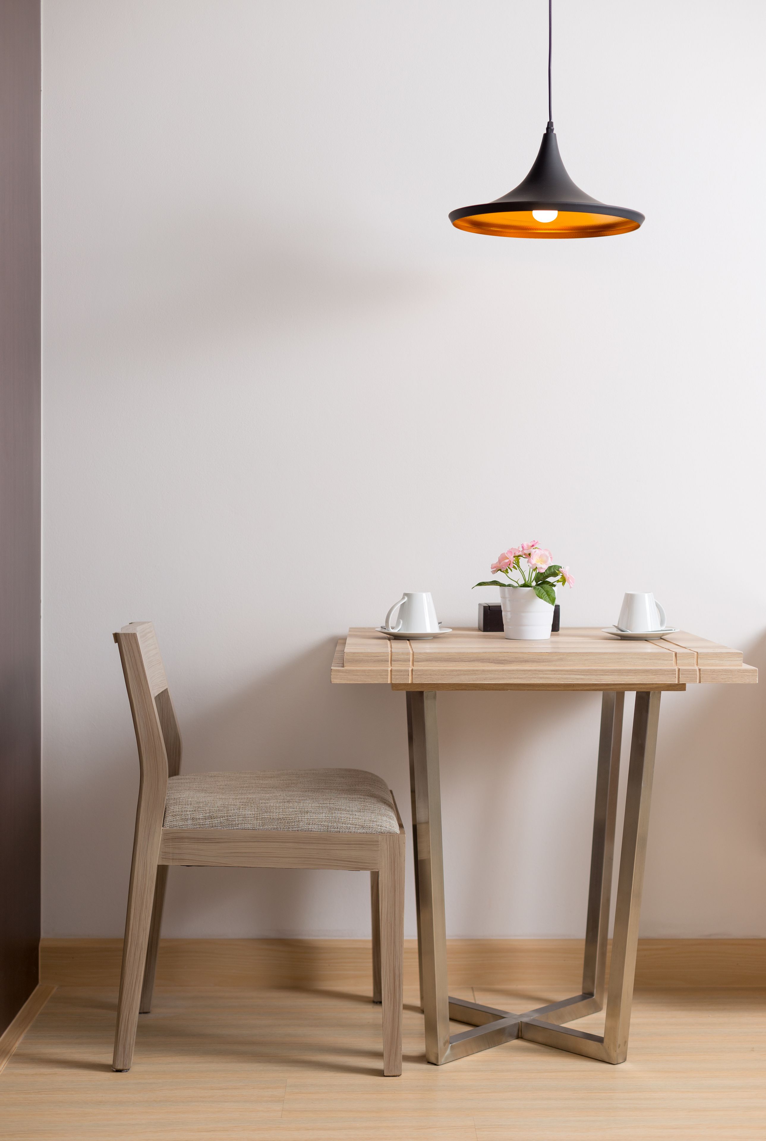 Un coin repas avec une table en bois, deux chaises, une suspension et une plante en pot.