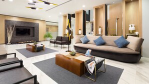 A modern living room with a sofa, coffee table, and chairs. There is a fireplace, a television, and a magazine rack. - The Canal 304 (Si Maha Phot)