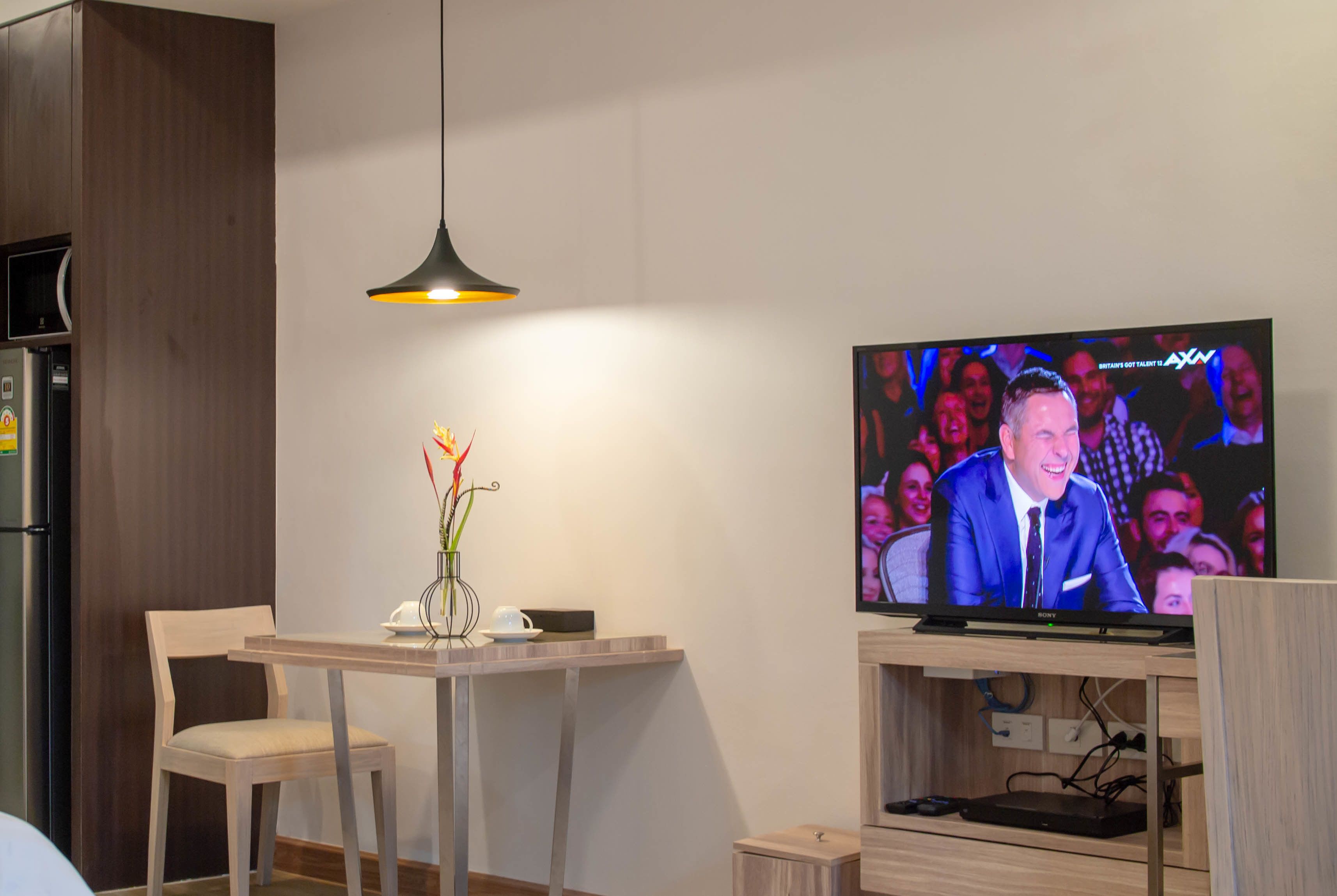 A modern living room with a flat-screen TV, wooden furniture, and a pendant light.