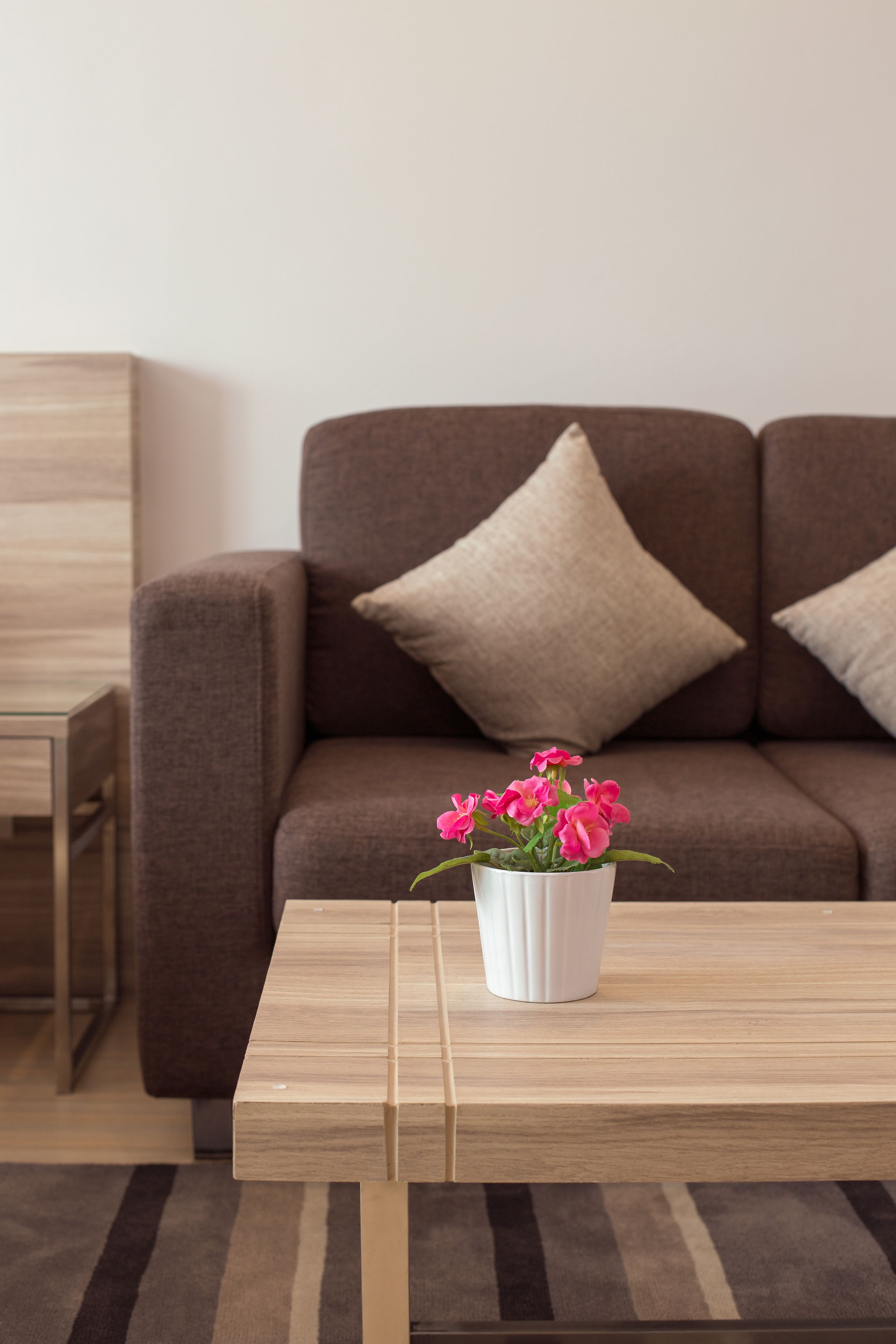 A modern living room with a brown sofa, a white coffee table, and a vase with pink flowers.