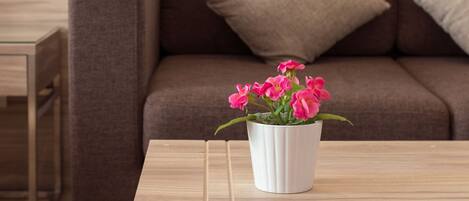 A modern living room with a brown sofa, a white coffee table, and a vase with pink flowers.