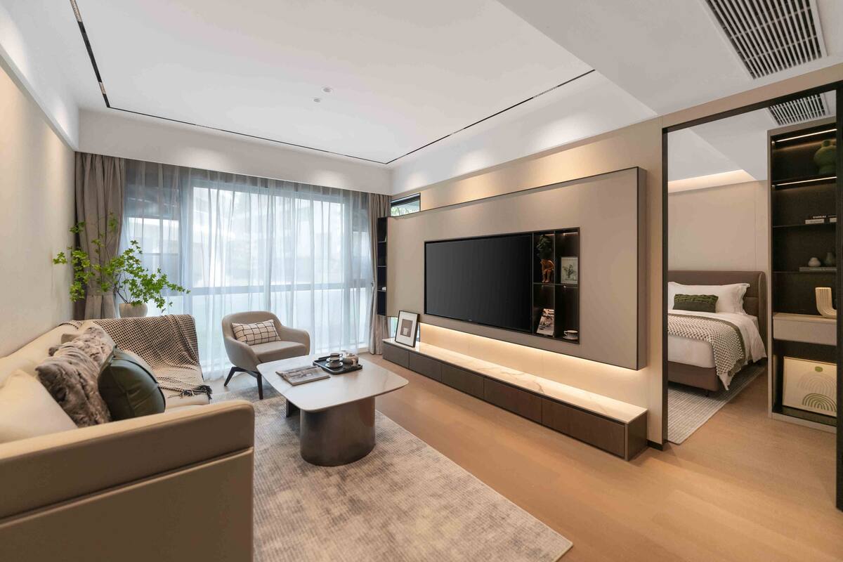 Ein modernes Wohnzimmer mit einer Couch, einem Sessel, einem Couchtisch und einem an der Wand befestigten Fernseher.