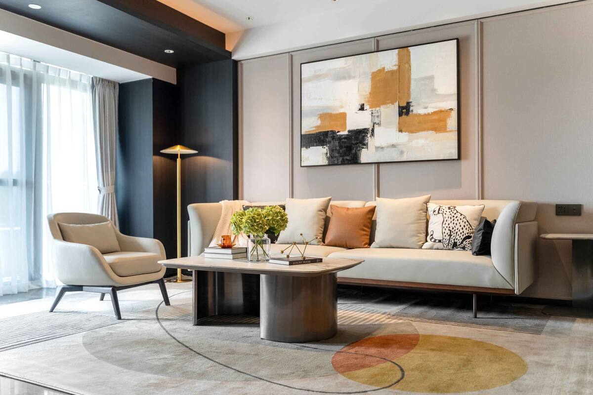 Ein modernes Wohnzimmer mit Sofa, Sessel und Couchtisch. An der Wand hängt ein großes abstraktes Gemälde und es steht eine Stehlampe im Raum.