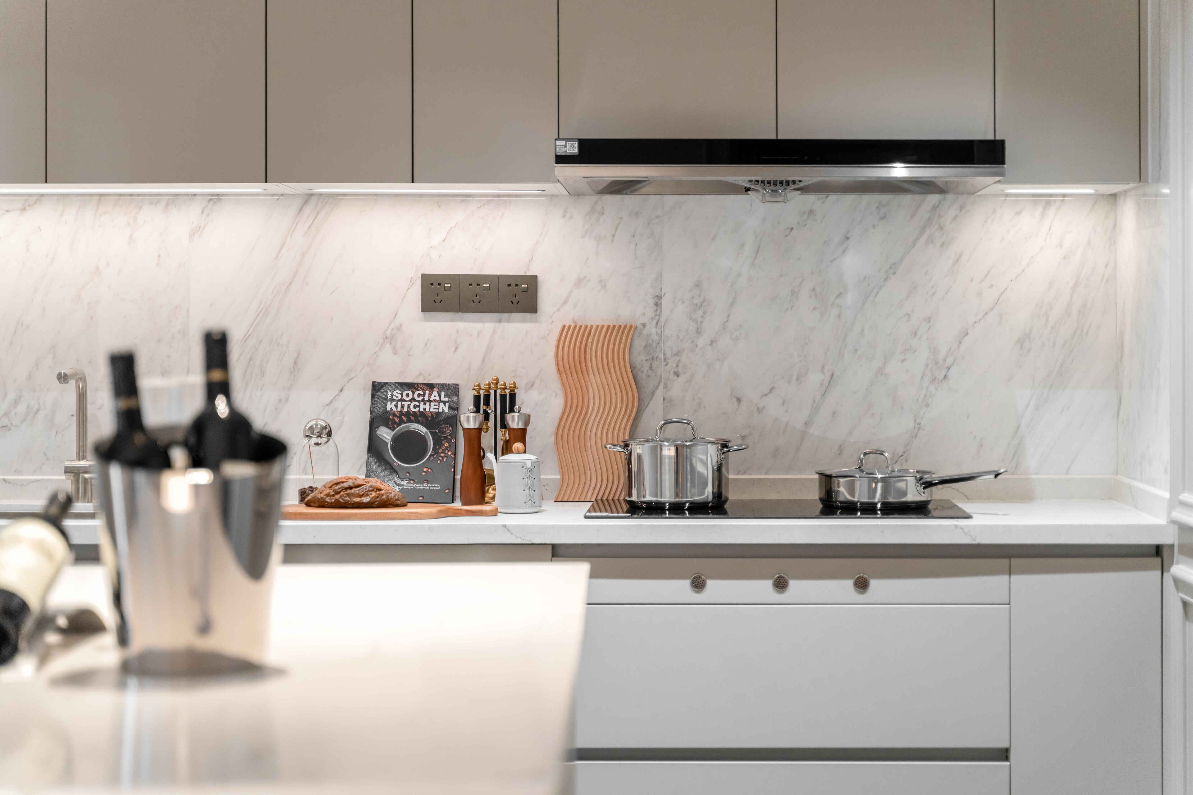 A modern kitchen with white cabinets, a marble backsplash, a built-in oven, and a pot on the stove.
