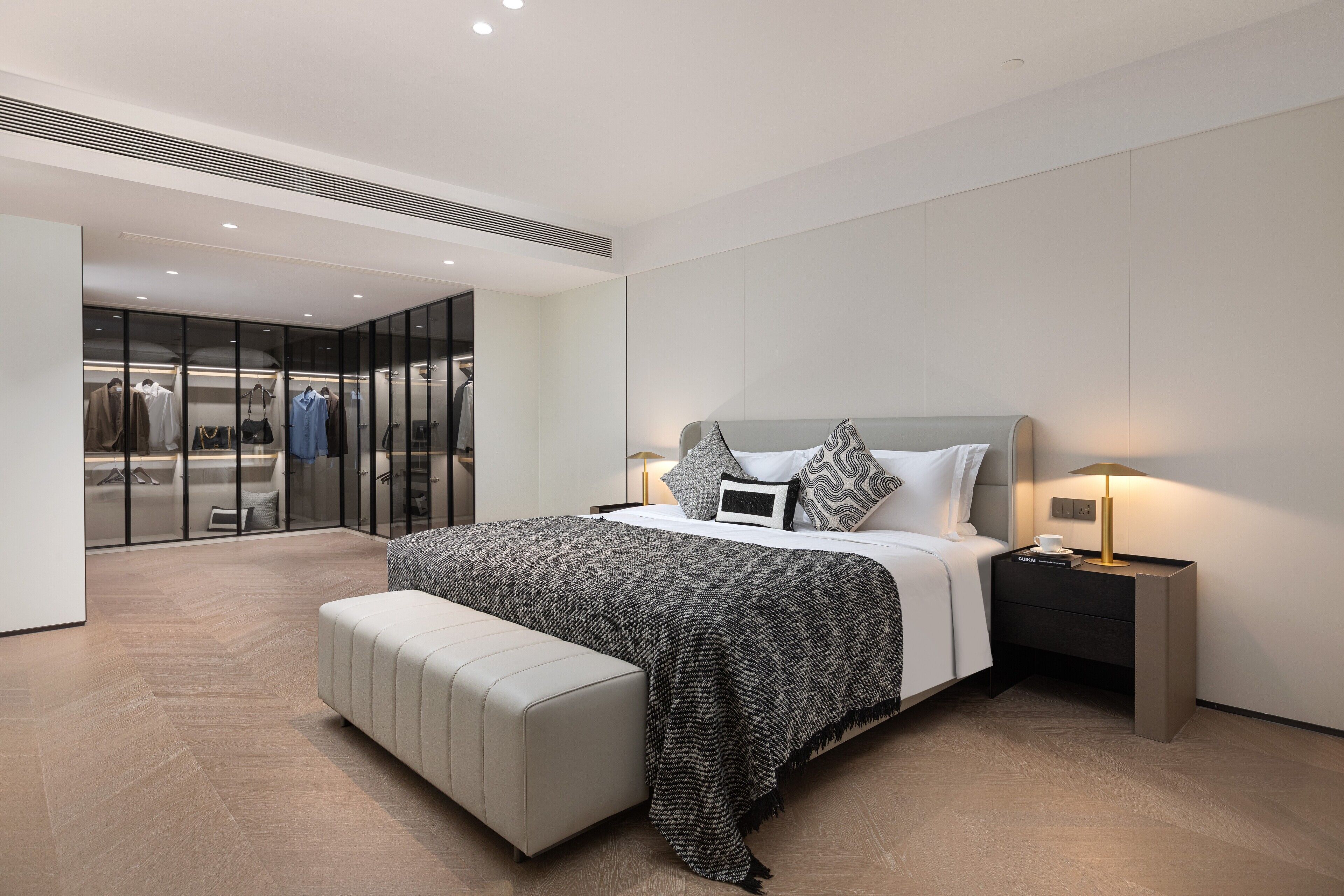 Quarto moderno com uma cama grande, um banco, uma mesa de cabeceira e um armário de vidro.