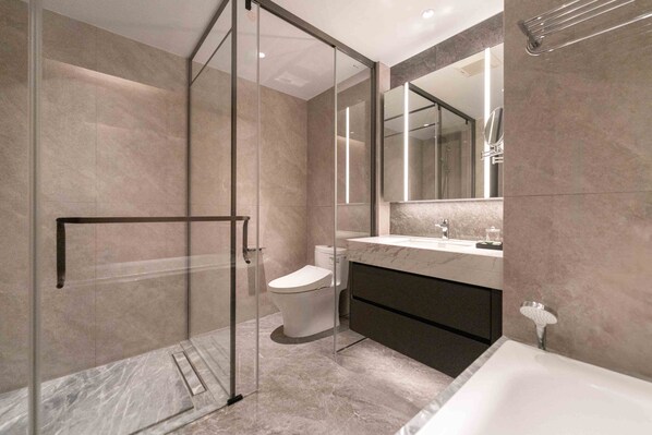 Un baño moderno con cabina de ducha de vidrio, inodoro, lavabo con espejo grande y bañera.