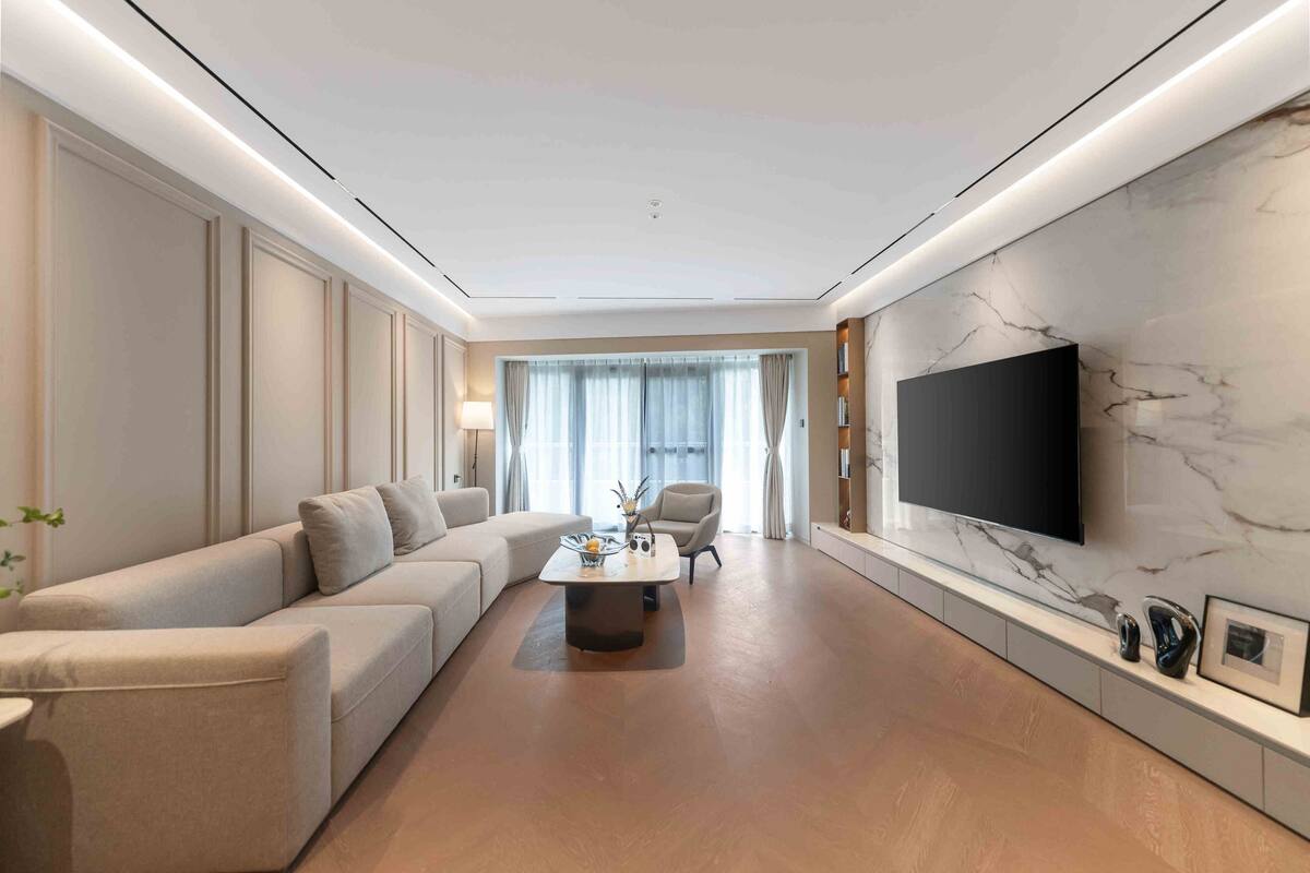 Ein modernes Wohnzimmer mit einem Ecksofa, einem Couchtisch, einem an der Wand montierten Flachbildfernseher und einer Wand mit Marmoroptik.