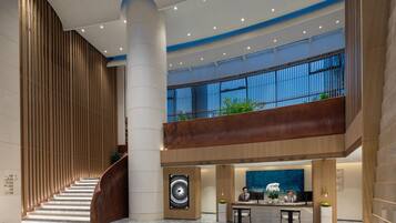 A modern hotel lobby with a central staircase, a reception desk, and a large blue artwork.