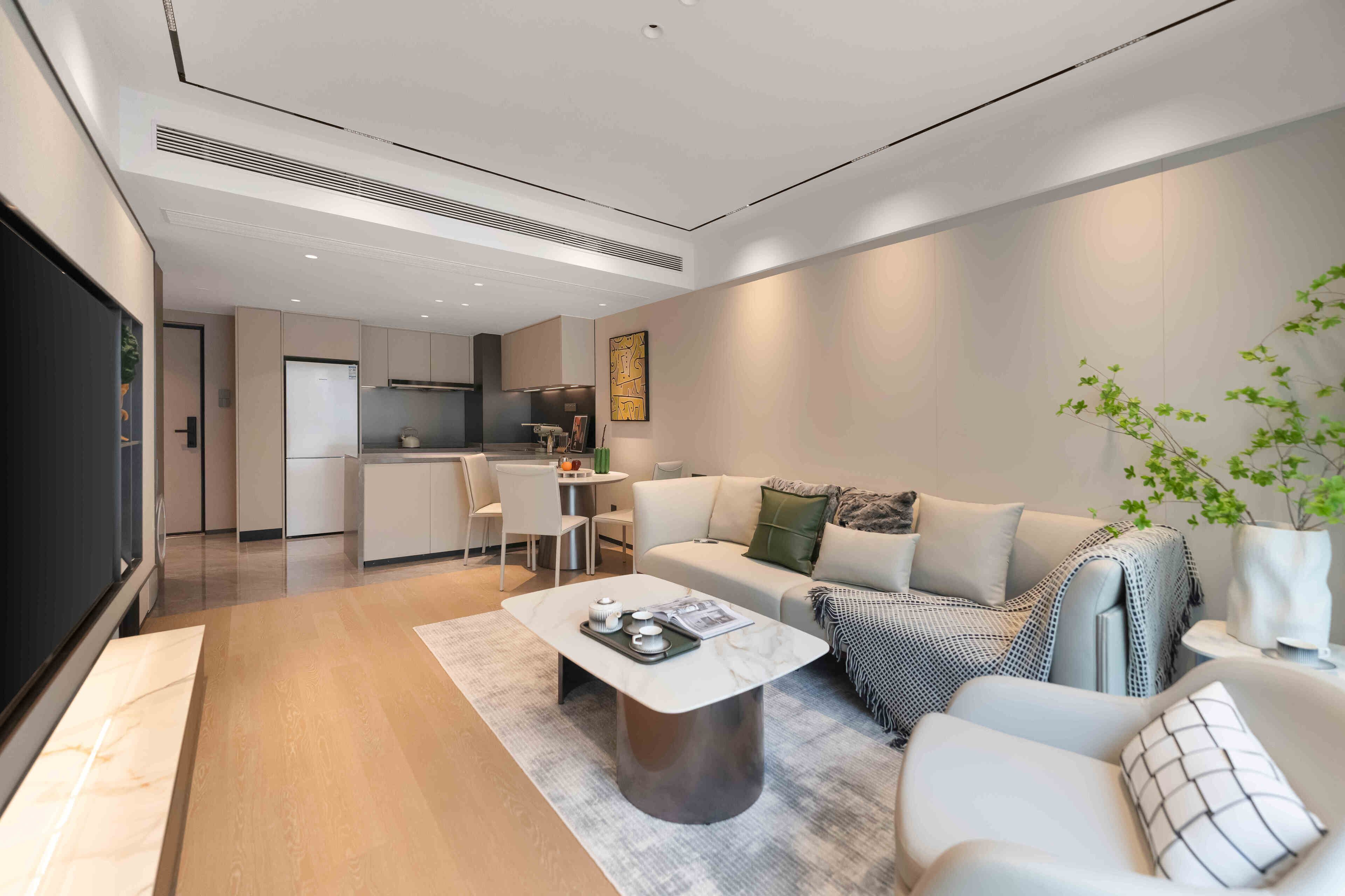 A modern living room with a sofa, armchair, and coffee table. There is a kitchen in the background with a dining area.