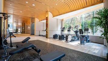 A modern gym with exercise equipment, large windows, and a wooden ceiling.